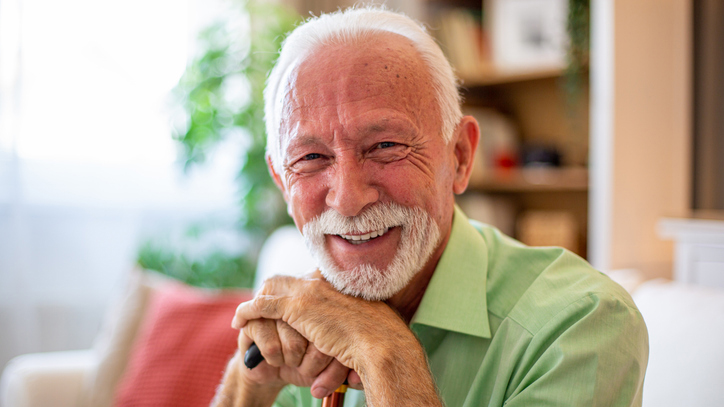 Happy senior man smiling and leaning on walking cane at home